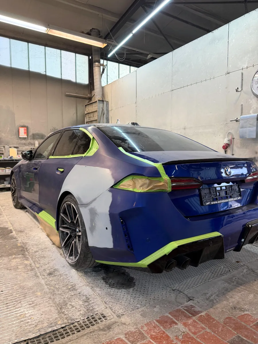 Blauer BMW 5er in der Lackierkabine, Heck und Seitenwand abgeklebt und grundiert